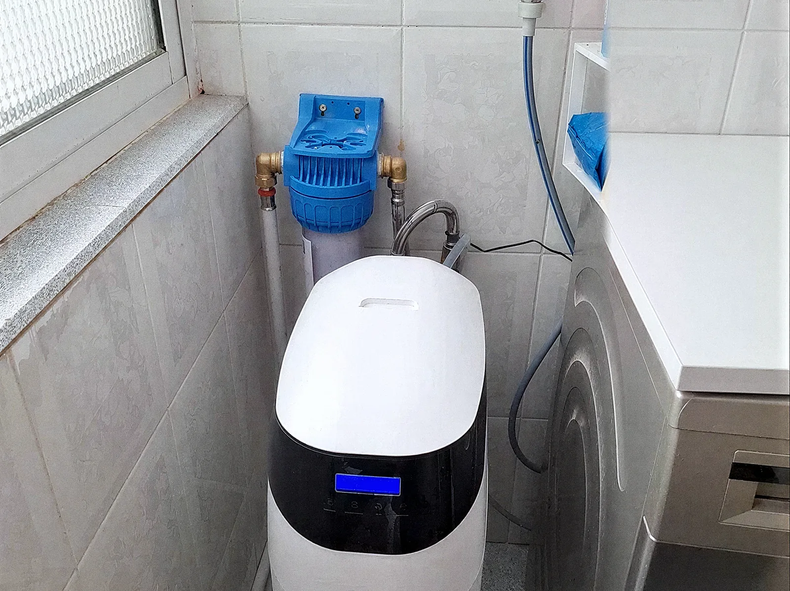 Descalcificador VD amb filtre de sediments blau instal·lat en un safareig enrajolat