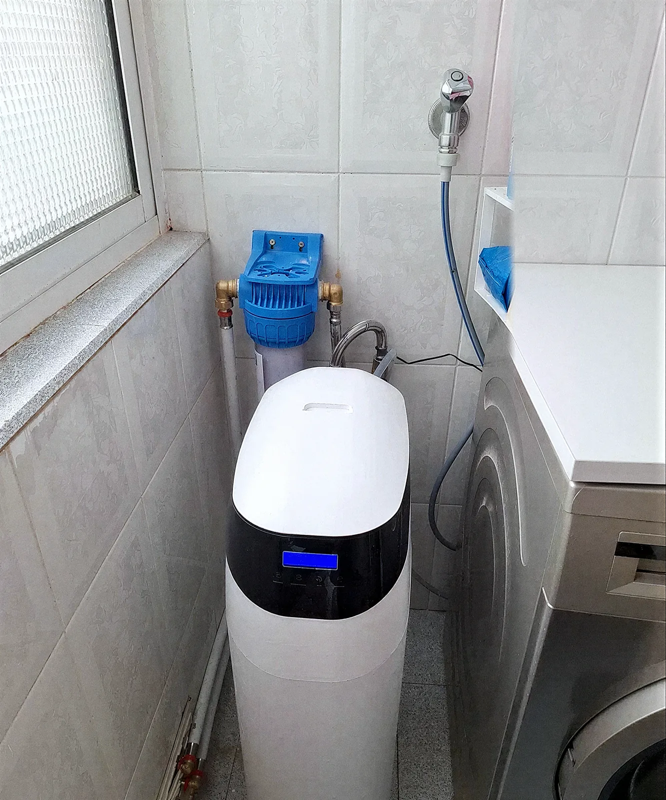 Descalcificador VD amb filtre de sediments blau instal·lat en un safareig enrajolat