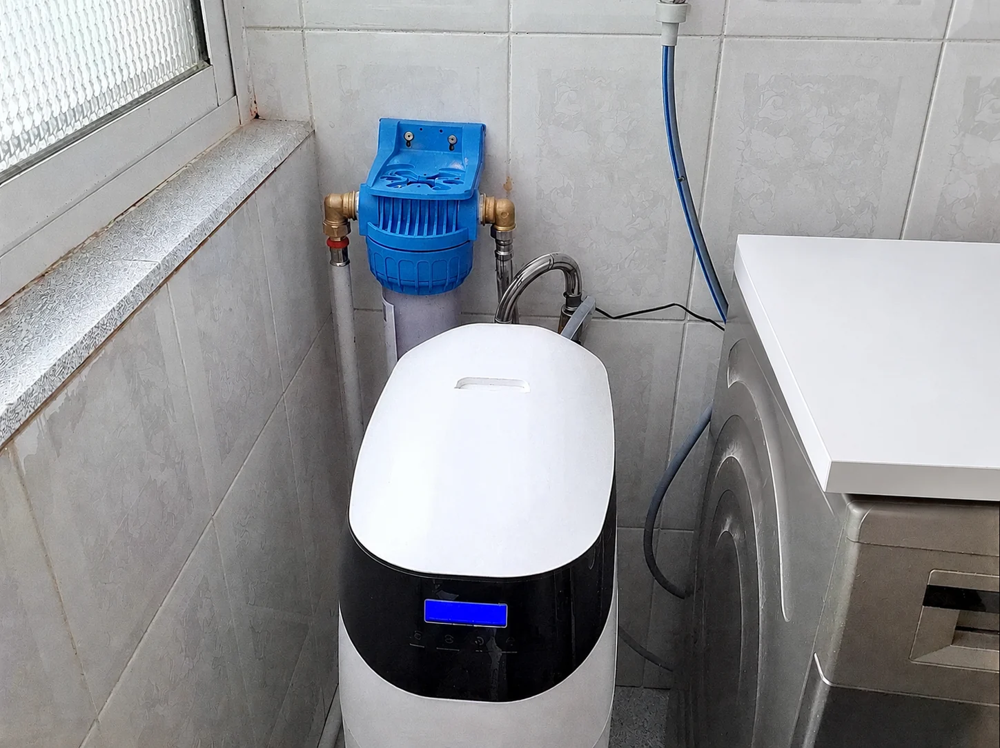Instalación de descalcificadores y ósmosis inversa: descalcificador con filtro de sedimentos junto a la lavadora en un lavadero de Barcelona